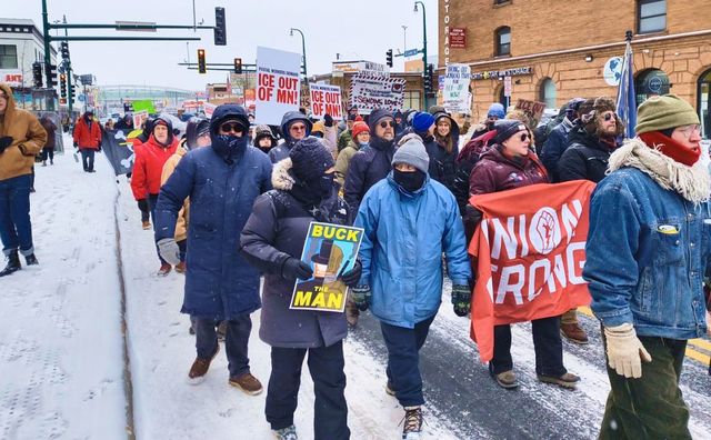 Protesters marching in winter holding signs including ICE OUT OF MN and UNION STRONG banners
