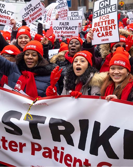 Nurses on strike wearing red beanies holding STRIKE banner and signs for fair contracts and better patient care